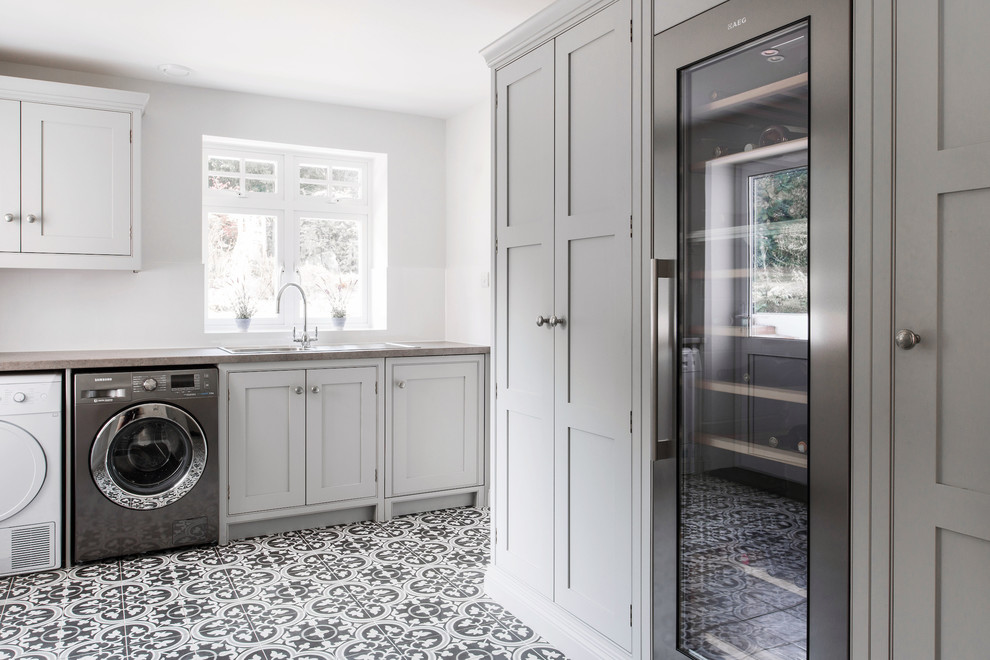 This is an example of an expansive contemporary u-shaped utility room in Kent with shaker cabinets, grey cabinets, ceramic floors, a side-by-side washer and dryer, a single-bowl sink, laminate benchtops, grey walls, yellow floor and grey benchtop.