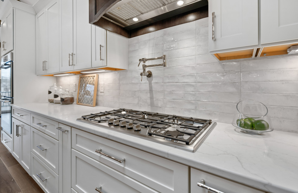 Open concept kitchen - transitional galley medium tone wood floor and vaulted ceiling open concept kitchen idea in Cincinnati with an undermount sink, shaker cabinets, white cabinets, quartz countertops, white backsplash, ceramic backsplash, stainless steel appliances, an island and white countertops