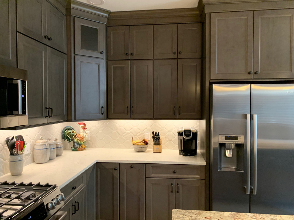Inspiration for a mid-sized transitional l-shaped medium tone wood floor and brown floor eat-in kitchen remodel in Cincinnati with an undermount sink, recessed-panel cabinets, gray cabinets, quartz countertops, white backsplash, porcelain backsplash, stainless steel appliances, an island and white countertops