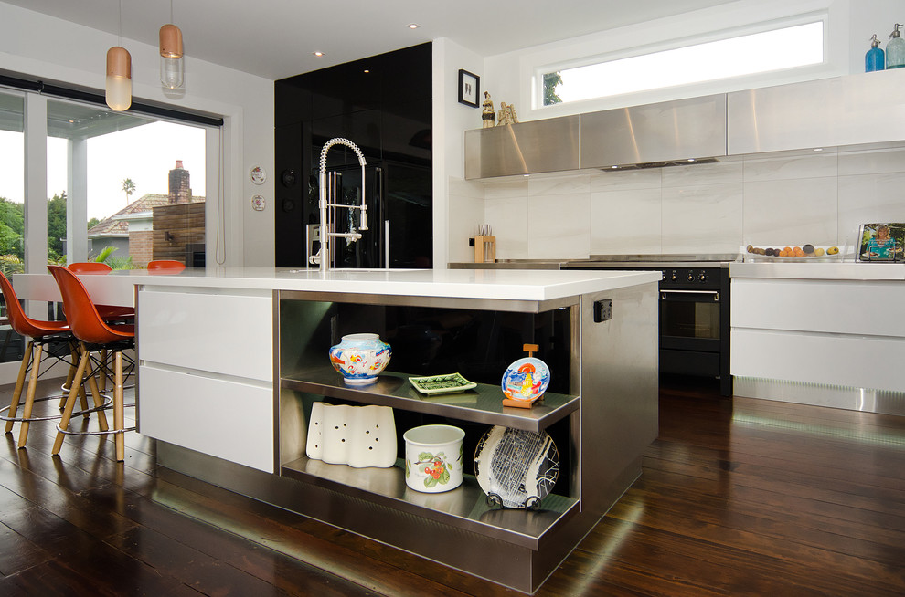 This is an example of a mid-sized contemporary galley eat-in kitchen in Auckland with an undermount sink, flat-panel cabinets, black cabinets, solid surface benchtops, grey splashback, stone tile splashback, black appliances, dark hardwood floors and with island.