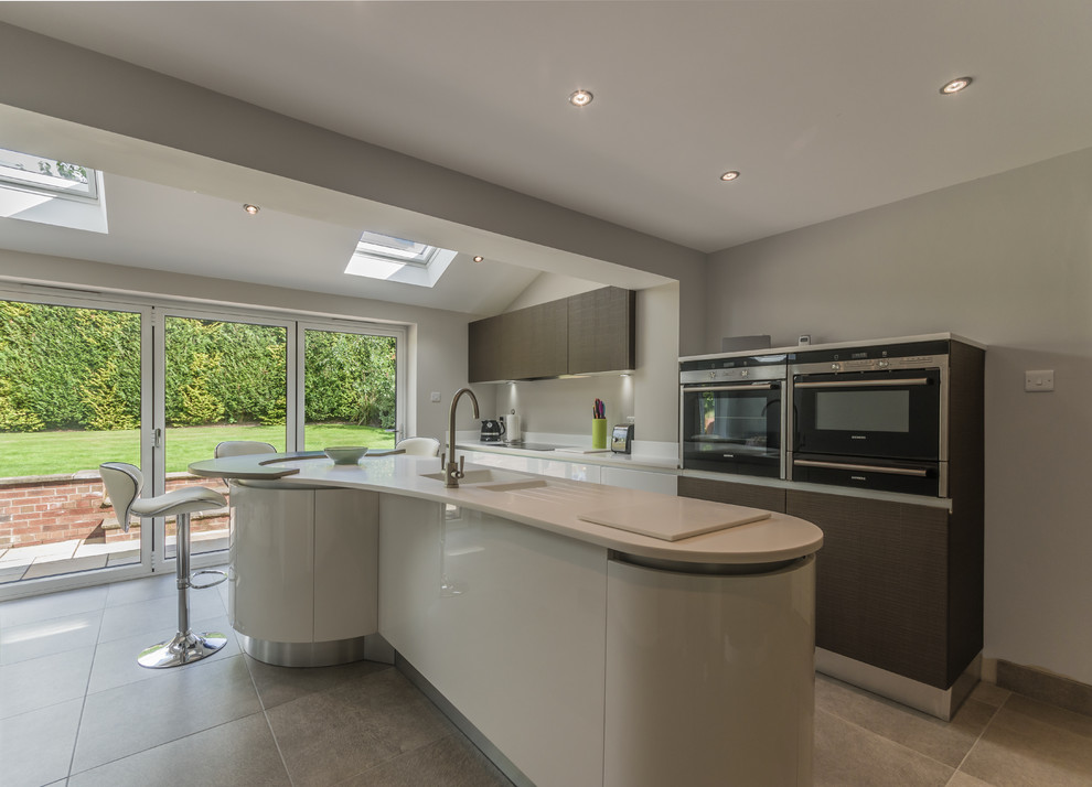 Inspiration for a large contemporary l-shaped open plan kitchen in Cheshire with a double-bowl sink, flat-panel cabinets, white cabinets, solid surface benchtops, porcelain floors and with island.