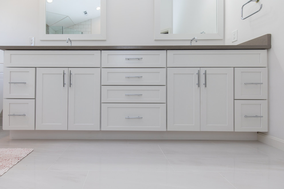 This is an example of a mid-sized transitional master bathroom in DC Metro with shaker cabinets, white cabinets, a freestanding tub, a corner shower, white tile, subway tile, white walls, porcelain floors, an undermount sink, solid surface benchtops, white floor and a hinged shower door.