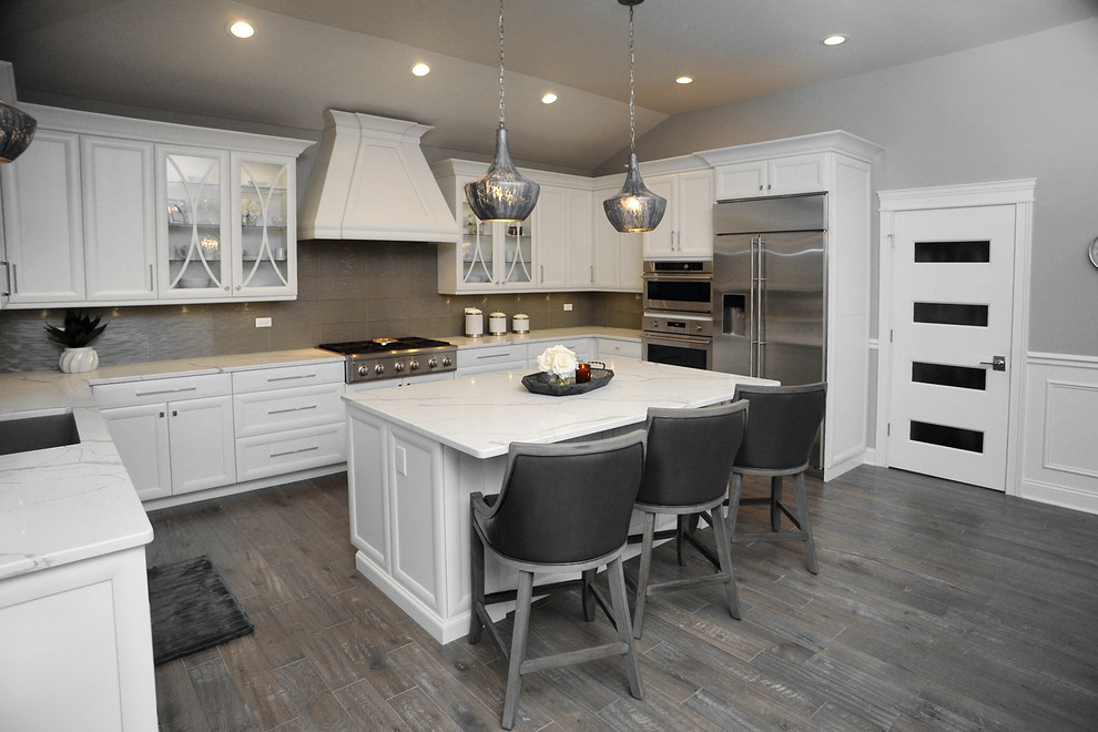 This is an example of a large traditional u-shaped eat-in kitchen in Chicago with an undermount sink, recessed-panel cabinets, white cabinets, quartzite benchtops, grey splashback, stainless steel appliances, laminate floors, with island, grey floor and white benchtop.