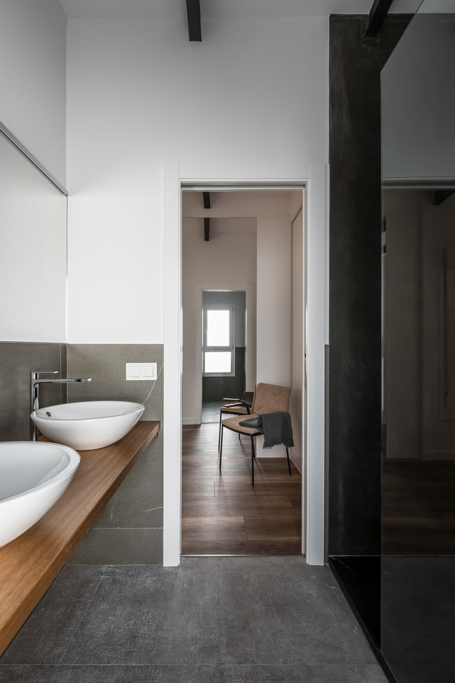 Diseño de cuarto de baño principal moderno con ducha a ras de suelo, baldosas y/o azulejos grises, baldosas y/o azulejos de porcelana, paredes blancas, suelo de baldosas de porcelana, lavabo sobreencimera, encimera de madera y suelo gris