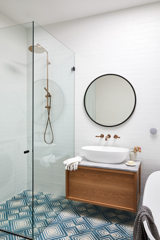 Design ideas for a mid-sized beach style master bathroom in Sydney with furniture-like cabinets, medium wood cabinets, a freestanding tub, an open shower, a wall-mount toilet, white tile, subway tile, white walls, cement tiles, a vessel sink, marble benchtops, blue floor, a hinged shower door, grey benchtops, a laundry, a single vanity, a floating vanity, recessed and brick walls.