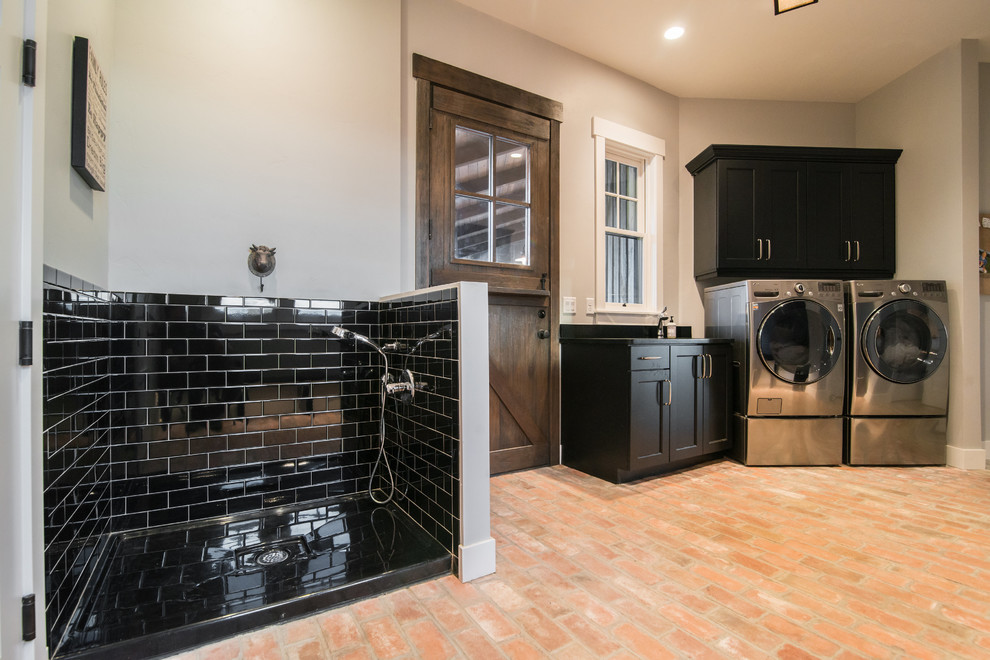 Large country l-shaped utility room in Denver with black cabinets, solid surface benchtops, grey walls, brick floors, a side-by-side washer and dryer, red floor and shaker cabinets.