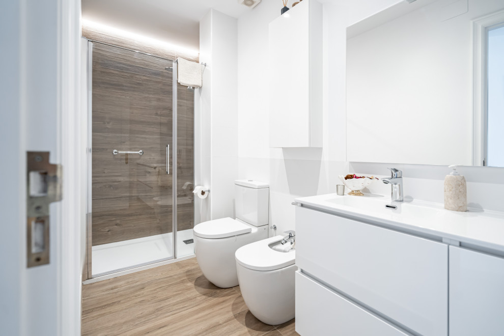 Example of a minimalist white tile and wood-look tile wood-look tile floor and single-sink bathroom design in Other with furniture-like cabinets, medium tone wood cabinets, a two-piece toilet, white walls, an integrated sink, solid surface countertops, a hinged shower door, white countertops and a built-in vanity