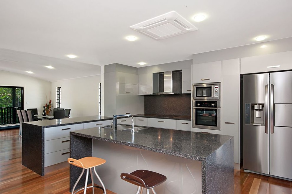 Photo of a large contemporary eat-in kitchen in Cairns with black splashback, stainless steel appliances, light hardwood floors and with island.