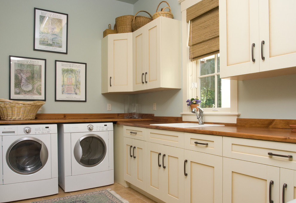 Photo of a mid-sized l-shaped dedicated laundry room in Atlanta with a drop-in sink, shaker cabinets, beige cabinets, wood benchtops, grey walls, ceramic floors, a side-by-side washer and dryer, beige floor and brown benchtop.