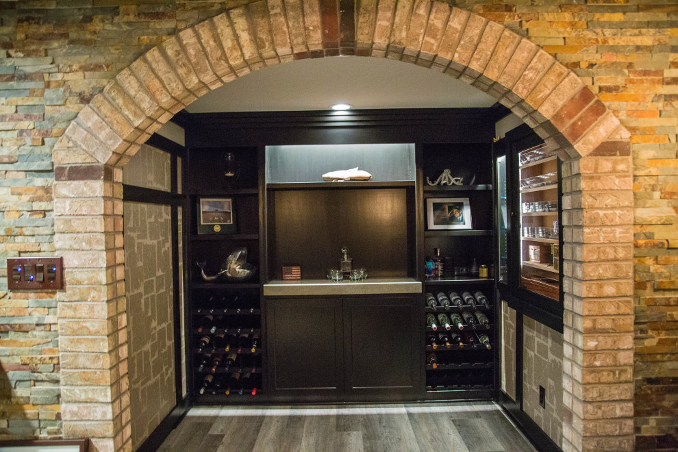 На фото: подземный, большой подвал с домашним баром, коричневыми стенами, полом из ламината, стандартным камином, фасадом камина из каменной кладки и коричневым полом с