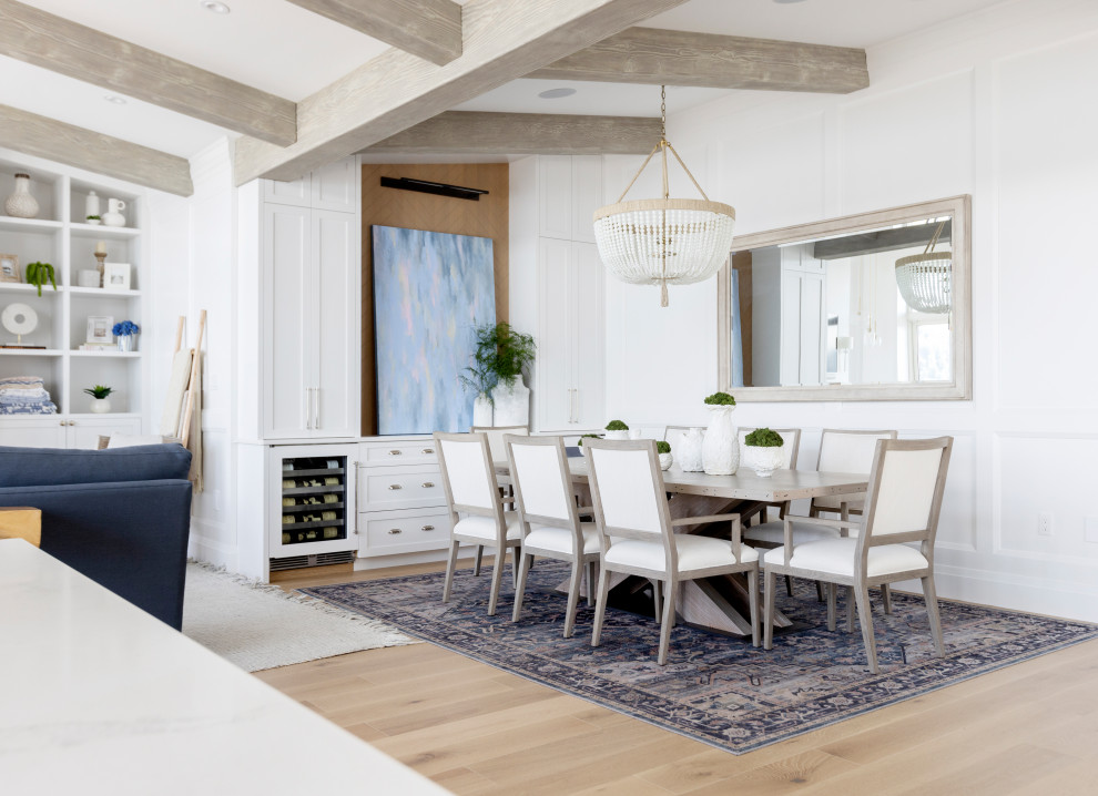 Foto di una sala da pranzo aperta verso il soggiorno stile marinaro con pareti bianche, parquet chiaro, pavimento beige, travi a vista e boiserie