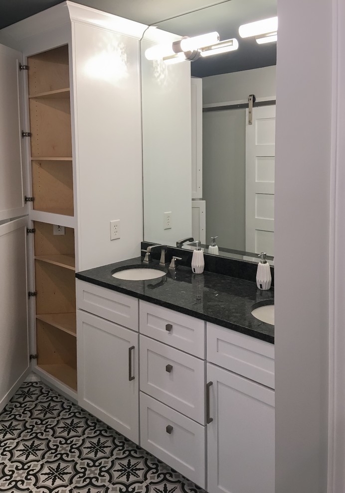 Inspiration for a mid-sized modern master bathroom in Other with shaker cabinets, white cabinets, a freestanding tub, a corner shower, gray tile, porcelain tile, grey walls, porcelain floors, an undermount sink, granite benchtops, a hinged shower door and black benchtops.