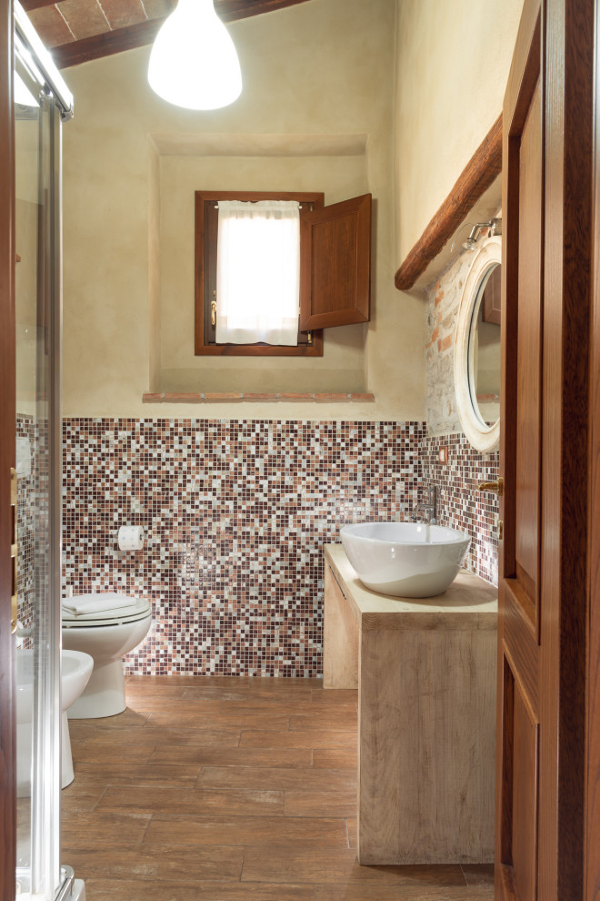 Inspiration för små rustika beige toaletter, med beige skåp, en toalettstol med separat cisternkåpa, flerfärgad kakel, mosaik, beige väggar, klinkergolv i porslin, ett fristående handfat, laminatbänkskiva och brunt golv