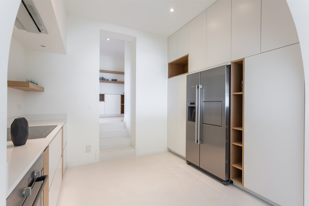 This is an example of an expansive scandinavian galley open plan kitchen in Paris with an undermount sink, beaded inset cabinets, solid surface benchtops, white splashback, stainless steel appliances, concrete floors and white floor.