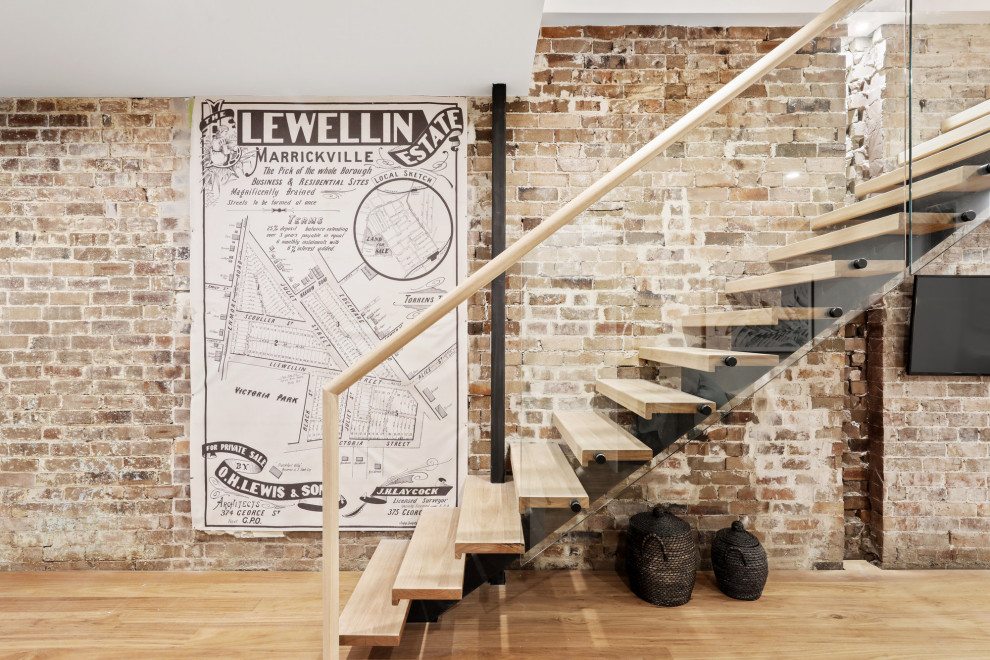 Réalisation d'un escalier sans contremarche design avec des marches en bois, un garde-corps en verre et un mur en parement de brique.