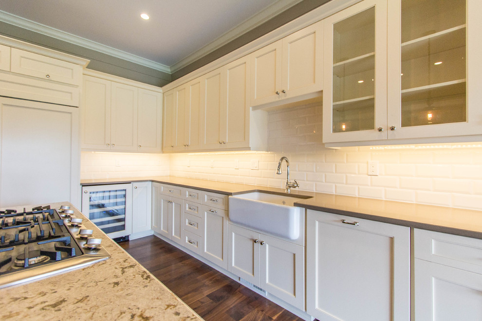 This is an example of a large traditional eat-in kitchen in Charleston with a farmhouse sink, white cabinets, granite benchtops, white splashback, panelled appliances, dark hardwood floors, with island and subway tile splashback.