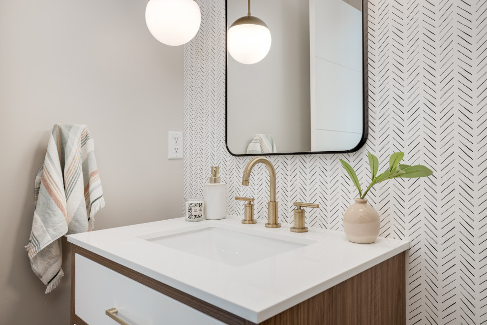 Small midcentury cloakroom in Minneapolis with flat-panel cabinets, medium wood cabinets, a wall mounted toilet, white walls, light hardwood flooring, a submerged sink, engineered stone worktops, beige floors, white worktops, a freestanding vanity unit and wallpapered walls.