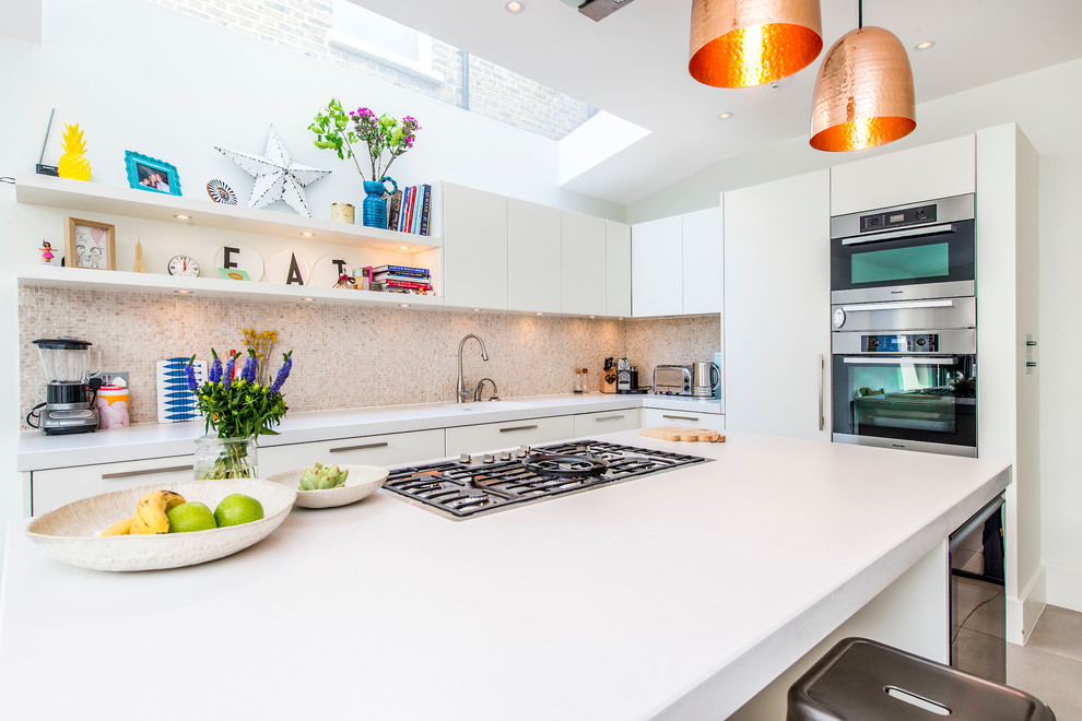 Photo of a large contemporary l-shaped eat-in kitchen in London with a drop-in sink, flat-panel cabinets, white cabinets, solid surface benchtops, beige splashback, mosaic tile splashback, stainless steel appliances, light hardwood floors and with island.