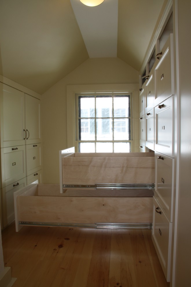 This is an example of a small traditional gender-neutral walk-in wardrobe in Portland Maine with shaker cabinets, white cabinets and medium hardwood floors.