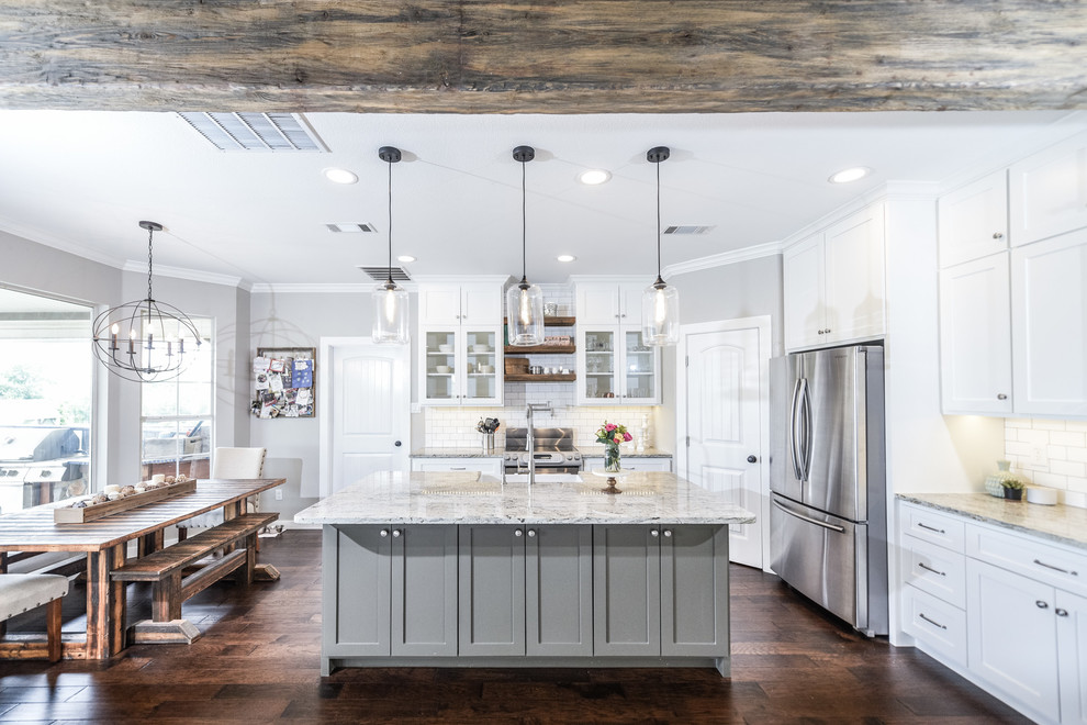 Design ideas for a country kitchen in Dallas with a farmhouse sink, shaker cabinets, white cabinets, granite benchtops, white splashback, ceramic splashback, stainless steel appliances, dark hardwood floors, with island and brown floor.