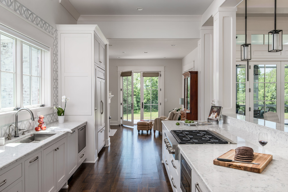 Open concept kitchen - transitional l-shaped dark wood floor and brown floor open concept kitchen idea in Nashville with an undermount sink, beaded inset cabinets, white cabinets, quartz countertops, white backsplash, stone tile backsplash, stainless steel appliances, an island and white countertops
