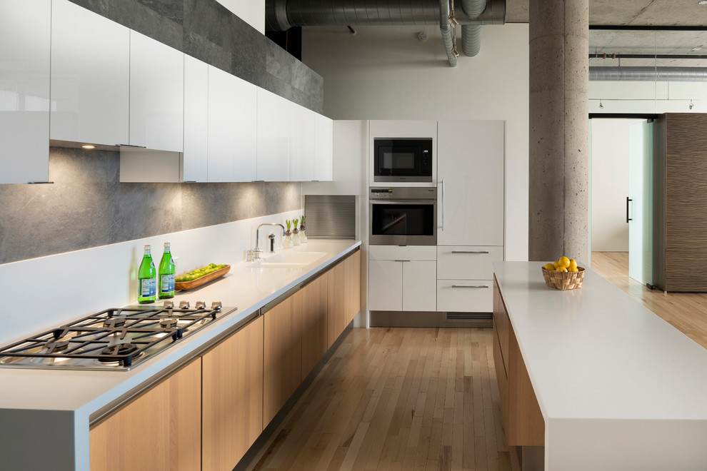 Photo of an industrial open plan kitchen in Minneapolis with flat-panel cabinets, light hardwood floors, with island, a double-bowl sink, white cabinets and stainless steel appliances.
