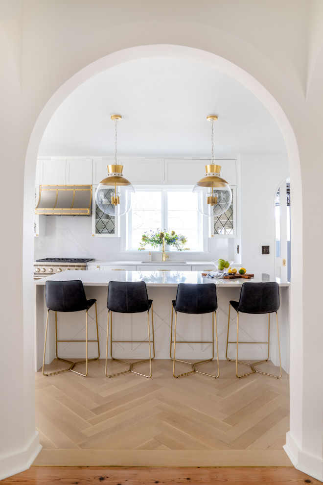 Photo of a large traditional l-shaped enclosed kitchen in New York with a submerged sink, recessed-panel cabinets, white cabinets, quartz worktops, white splashback, engineered quartz splashback, integrated appliances, light hardwood flooring, an island, beige floors and white worktops.