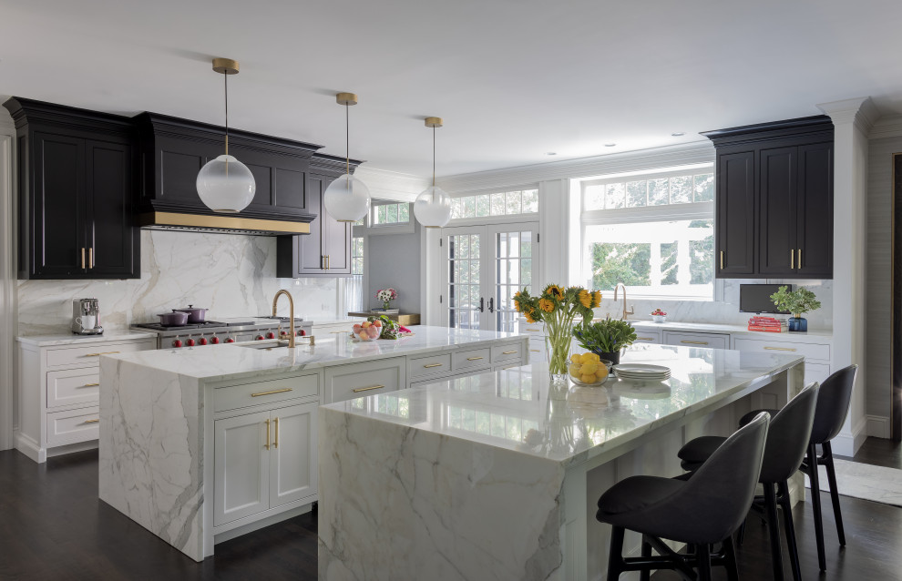 This is an example of a large transitional separate kitchen in Boston with a farmhouse sink, shaker cabinets, black cabinets, marble benchtops, white splashback, stone slab splashback, stainless steel appliances, dark hardwood floors, multiple islands, brown floor and white benchtop.