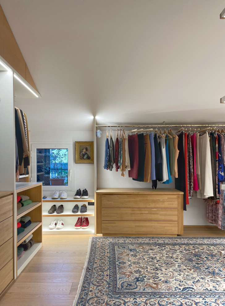 Diseño de armario vestidor unisex actual extra grande con armarios abiertos, puertas de armario de madera clara y suelo de madera clara