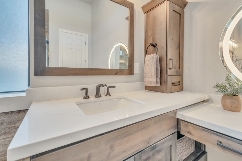 This is an example of a large transitional master bathroom in Phoenix with recessed-panel cabinets, brown cabinets, a freestanding tub, an open shower, white tile, ceramic tile, grey walls, porcelain floors, an undermount sink, quartzite benchtops, beige floor, a hinged shower door, white benchtops, a double vanity and a built-in vanity.