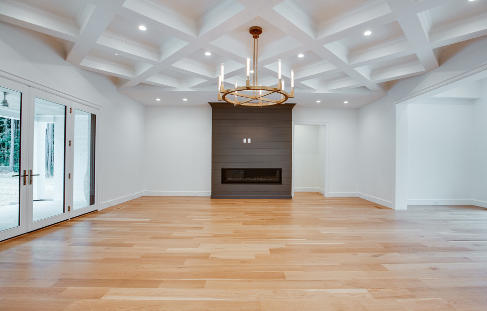 This is an example of a large classic open plan games room in Charlotte with white walls, light hardwood flooring, a standard fireplace, a timber clad chimney breast, yellow floors and a coffered ceiling.