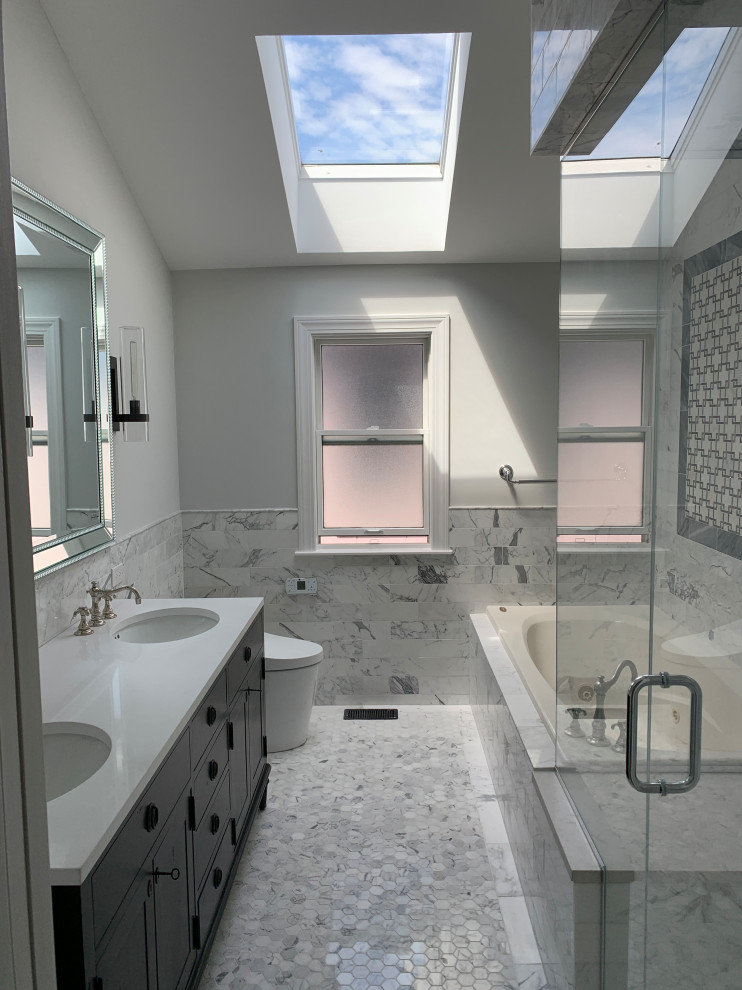 This is an example of a large transitional master bathroom in Chicago with furniture-like cabinets, black cabinets, a drop-in tub, a corner shower, a bidet, white tile, marble, grey walls, marble floors, an undermount sink, engineered quartz benchtops, grey floor, a hinged shower door, white benchtops, a shower seat, a double vanity, a freestanding vanity and vaulted.