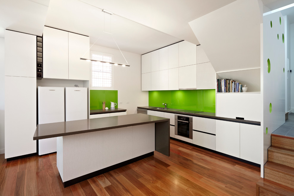Inspiration for a contemporary kitchen in Melbourne with an undermount sink, flat-panel cabinets, white cabinets, green splashback, glass sheet splashback, stainless steel appliances, medium hardwood floors and with island.