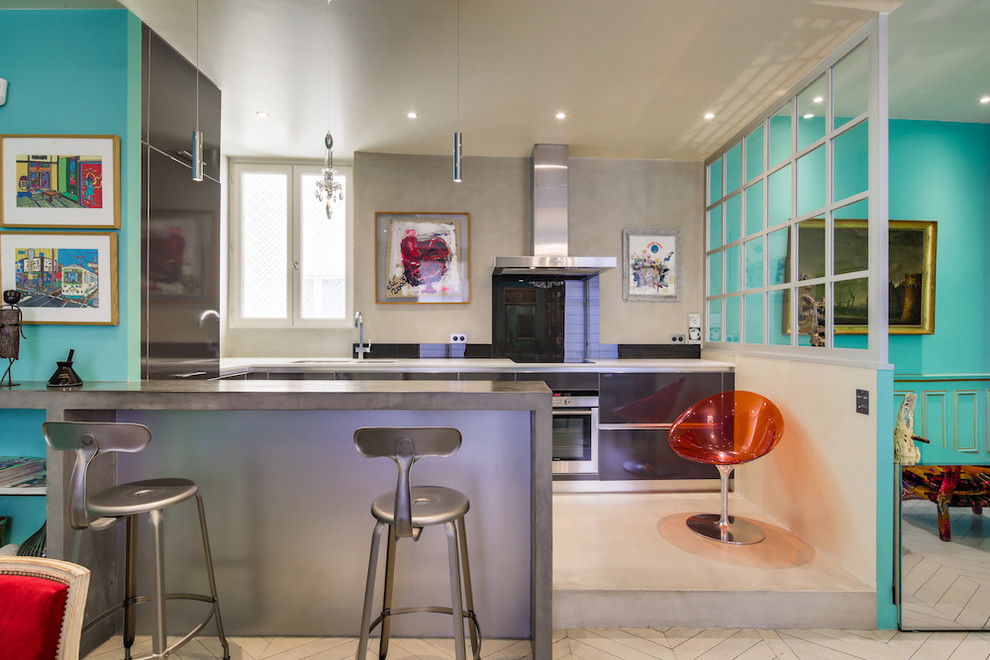 Design ideas for a small eclectic l-shaped eat-in kitchen in Paris with grey floor, an undermount sink, flat-panel cabinets, grey cabinets, solid surface benchtops, black splashback, glass sheet splashback, stainless steel appliances, concrete floors, no island and white benchtop.