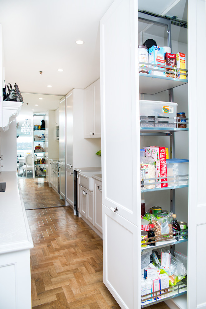 Design ideas for a mid-sized traditional galley eat-in kitchen in Sydney with a farmhouse sink, recessed-panel cabinets, white cabinets, quartz benchtops, white splashback, stone slab splashback, panelled appliances, light hardwood floors, no island and brown floor.