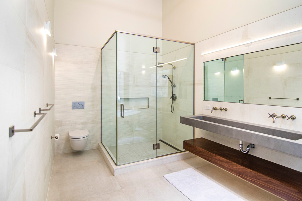 Large industrial master bathroom in New York with flat-panel cabinets, medium wood cabinets, a freestanding tub, a corner shower, a wall-mount toilet, beige tile, porcelain tile, white walls, ceramic floors, a wall-mount sink, concrete benchtops, beige floor, a hinged shower door and grey benchtops.