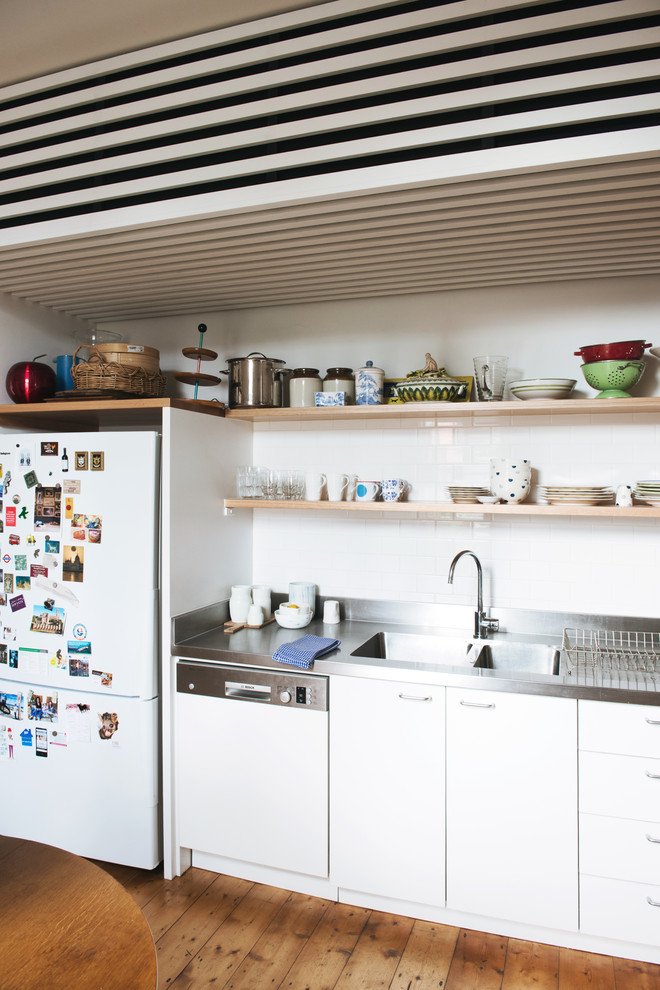 Mid-sized scandinavian l-shaped kitchen in Melbourne with a double-bowl sink, beaded inset cabinets, white cabinets, stainless steel benchtops, white splashback, ceramic splashback, stainless steel appliances, light hardwood floors and no island.