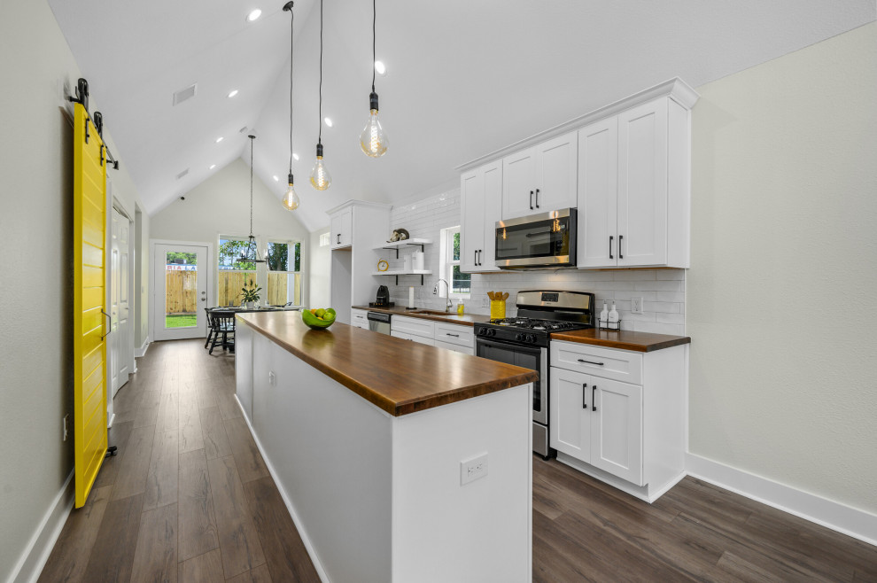 Bild på ett mellanstort funkis brun linjärt brunt kök och matrum, med en undermonterad diskho, luckor med upphöjd panel, vita skåp, träbänkskiva, vitt stänkskydd, stänkskydd i keramik, rostfria vitvaror, laminatgolv, en köksö och grått golv
