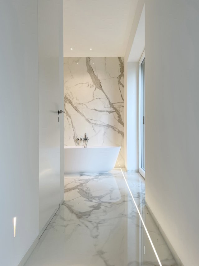 Пример оригинального дизайна: огромная главная ванная комната в современном стиле с плоскими фасадами, белыми фасадами, отдельно стоящей ванной, душем без бортиков, инсталляцией, белой плиткой, мраморной плиткой, белыми стенами, мраморным полом, подвесной раковиной, мраморной столешницей, белым полом, белой столешницей, нишей, тумбой под две раковины, подвесной тумбой, потолком с обоями и обоями на стенах