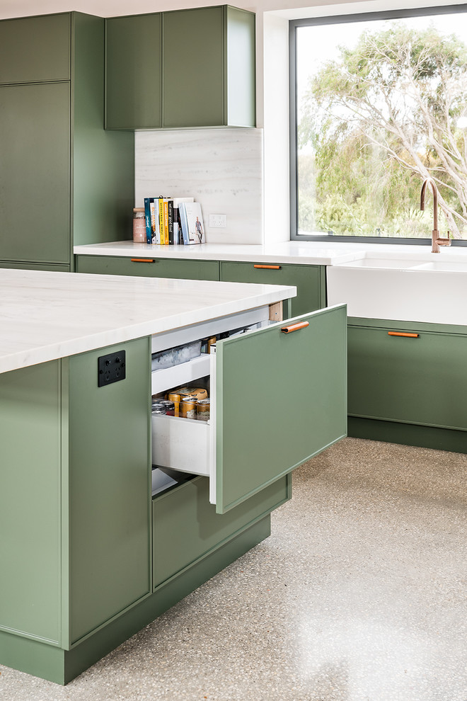 Large contemporary l-shaped open plan kitchen in Melbourne with a farmhouse sink, shaker cabinets, green cabinets, marble benchtops, white splashback, marble splashback, black appliances, concrete floors, with island, grey floor and white benchtop.