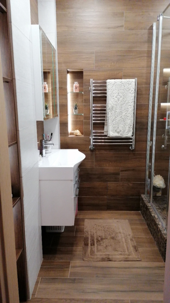 Идея дизайна: маленькая ванная комната с белыми фасадами, угловым душем, коричневой плиткой, удлиненной плиткой, коричневыми стенами, полом из керамогранита, душевой кабиной, подвесной раковиной, коричневым полом, душем с распашными дверями, зеркалом с подсветкой, тумбой под одну раковину и подвесной тумбой для на участке и в саду