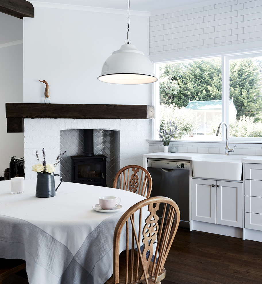 This is an example of a country single-wall eat-in kitchen in Melbourne with a farmhouse sink, shaker cabinets, white cabinets, white splashback, subway tile splashback, stainless steel appliances, dark hardwood floors and no island.