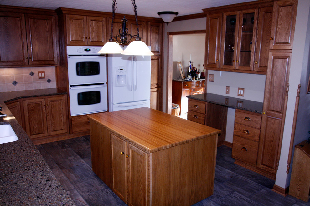 Mid-sized l-shaped eat-in kitchen photo with an undermount sink, raised-panel cabinets, medium tone wood cabinets, quartz countertops, beige backsplash, stone tile backsplash, white appliances and an island