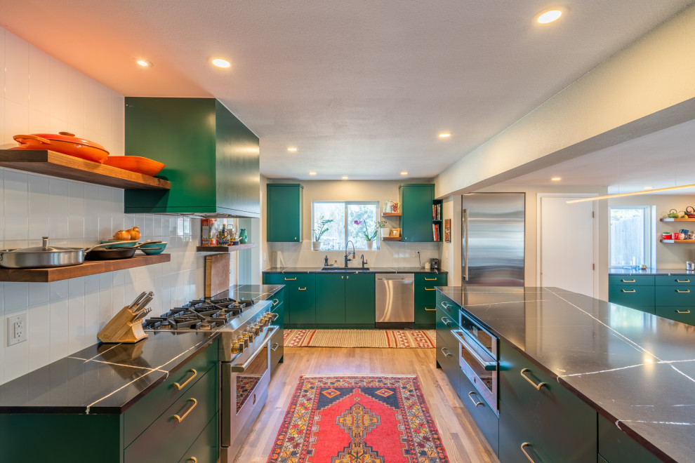 Large mid-century modern medium tone wood floor and brown floor kitchen photo in Denver with an undermount sink, flat-panel cabinets, green cabinets, granite countertops, white backsplash, subway tile backsplash, stainless steel appliances, an island and black countertops