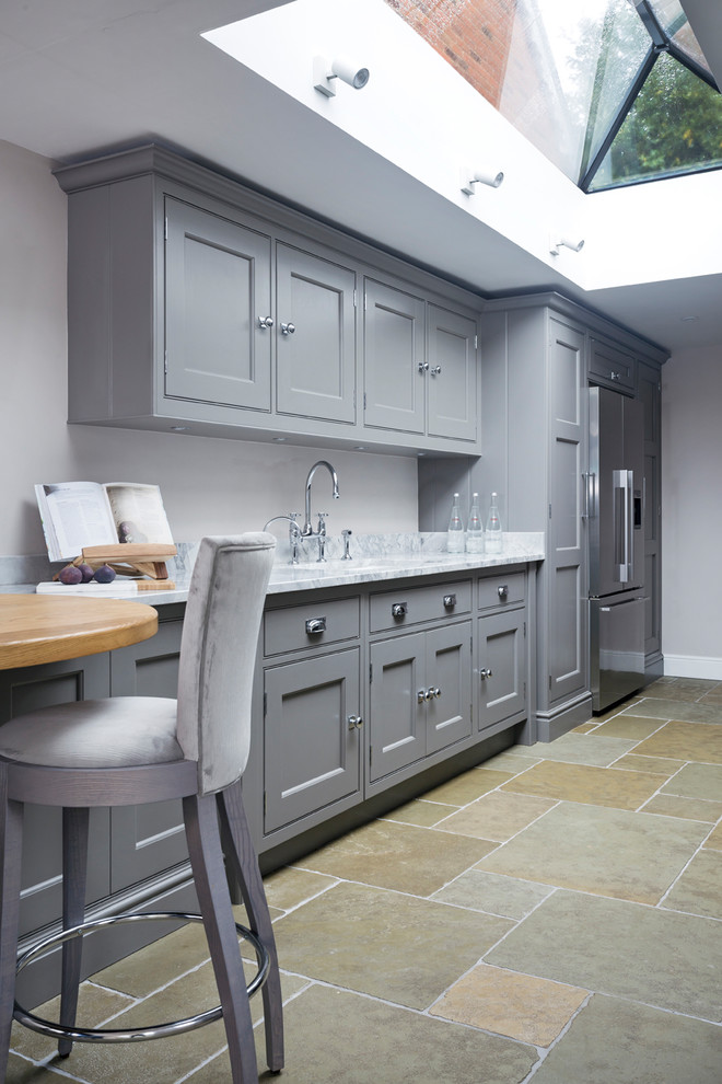 This is an example of a small traditional galley eat-in kitchen in Hampshire with a double-bowl sink, flat-panel cabinets, grey cabinets, marble benchtops, mirror splashback, stainless steel appliances, limestone floors, no island and beige floor.