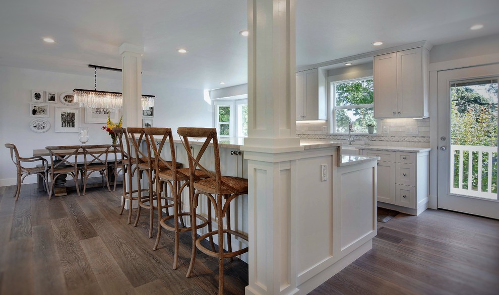 Photo of a mid-sized beach style galley eat-in kitchen in Seattle with a farmhouse sink, shaker cabinets, white cabinets, marble benchtops, white splashback, stone tile splashback, stainless steel appliances, medium hardwood floors and with island.