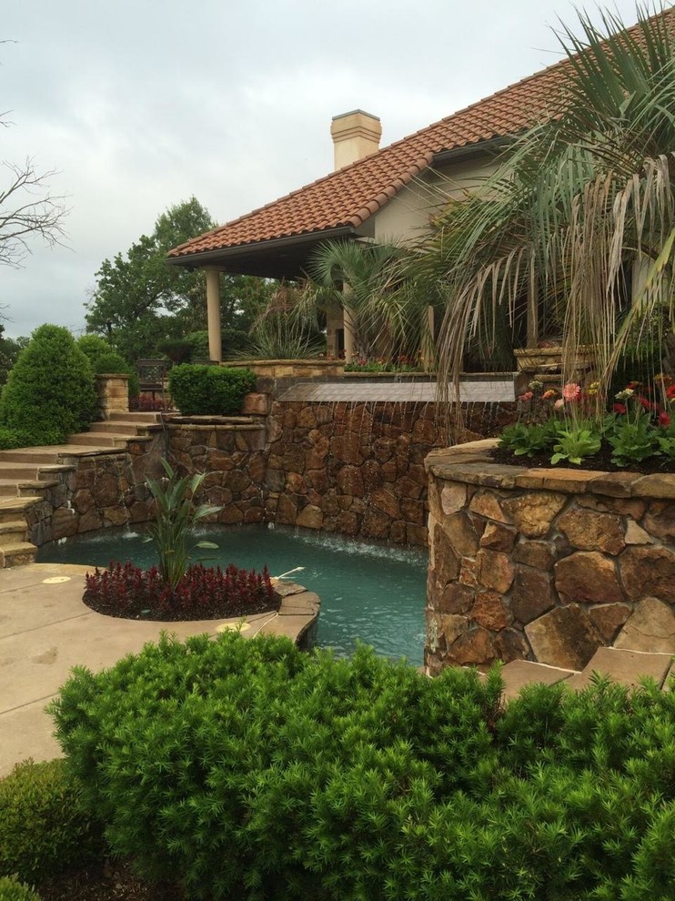 Photo of a large tropical backyard kidney-shaped pool in Dallas with a water feature and concrete slab.
