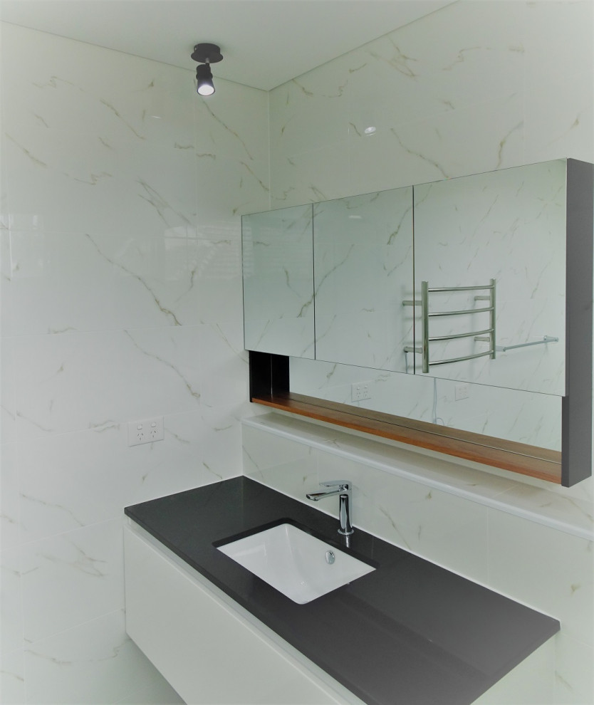 This is an example of a mid-sized contemporary bathroom in Sydney with white cabinets, white tile, ceramic tile, solid surface benchtops, black benchtops, a single vanity and a floating vanity.