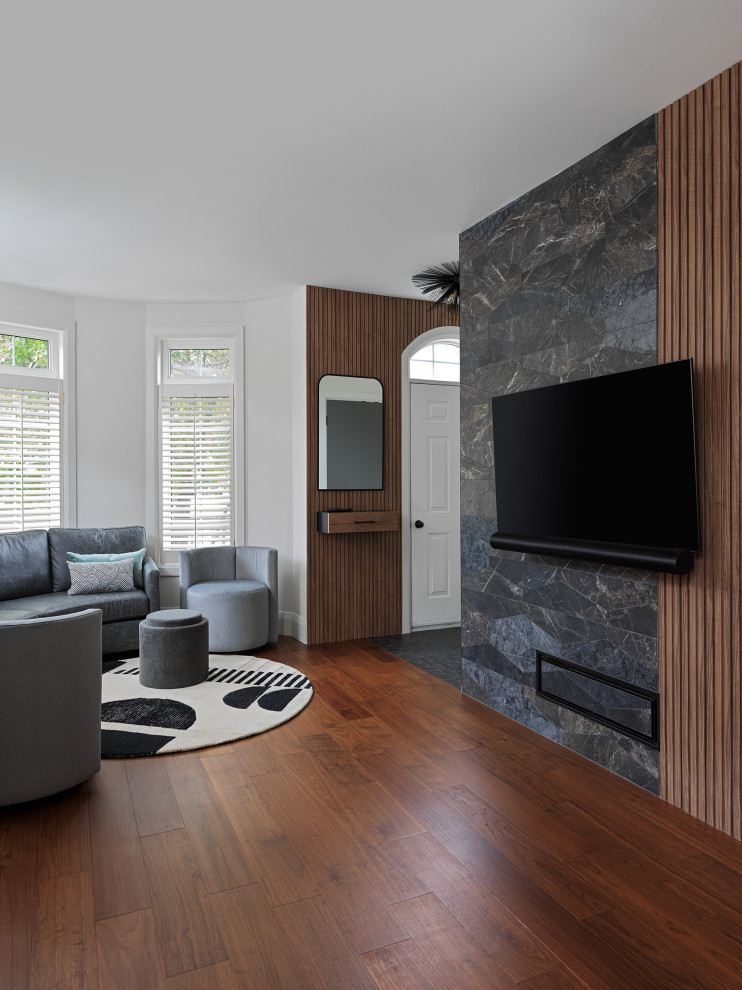 Cette photo montre un petit salon tendance en bois ouvert avec un mur gris, un sol en bois brun, aucune cheminée, un téléviseur fixé au mur et un sol marron.