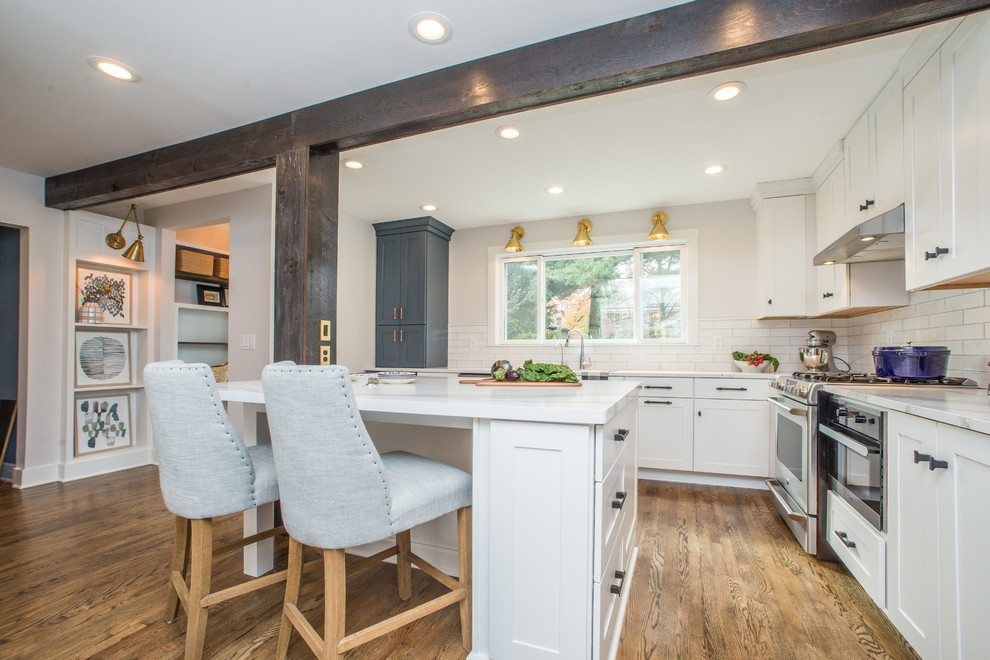 Beach style l-shaped kitchen in Other with shaker cabinets, white cabinets, white splashback, stainless steel appliances, medium hardwood floors, with island and white benchtop.